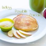A pancake on a white plate with sliced apples and apple sauce in a small green bowl.