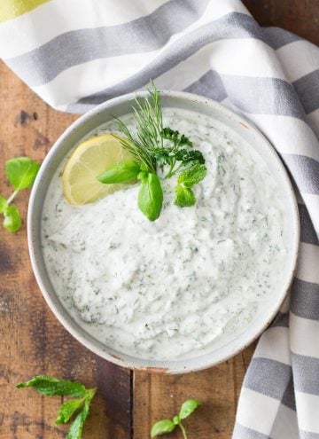 Bowl of Quark Dip viewed from the top garnished with herbs and sliced lemon on a wooden board and a grey and white napkin.