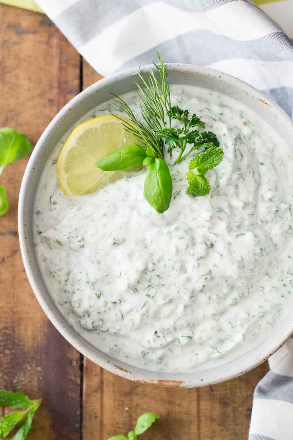 Bowl of Quark Dip viewed from the top garnished with herbs and sliced lemon on a wooden board and a grey and white napkin.