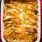 Red casserole dish with sweet potato gratin in it.