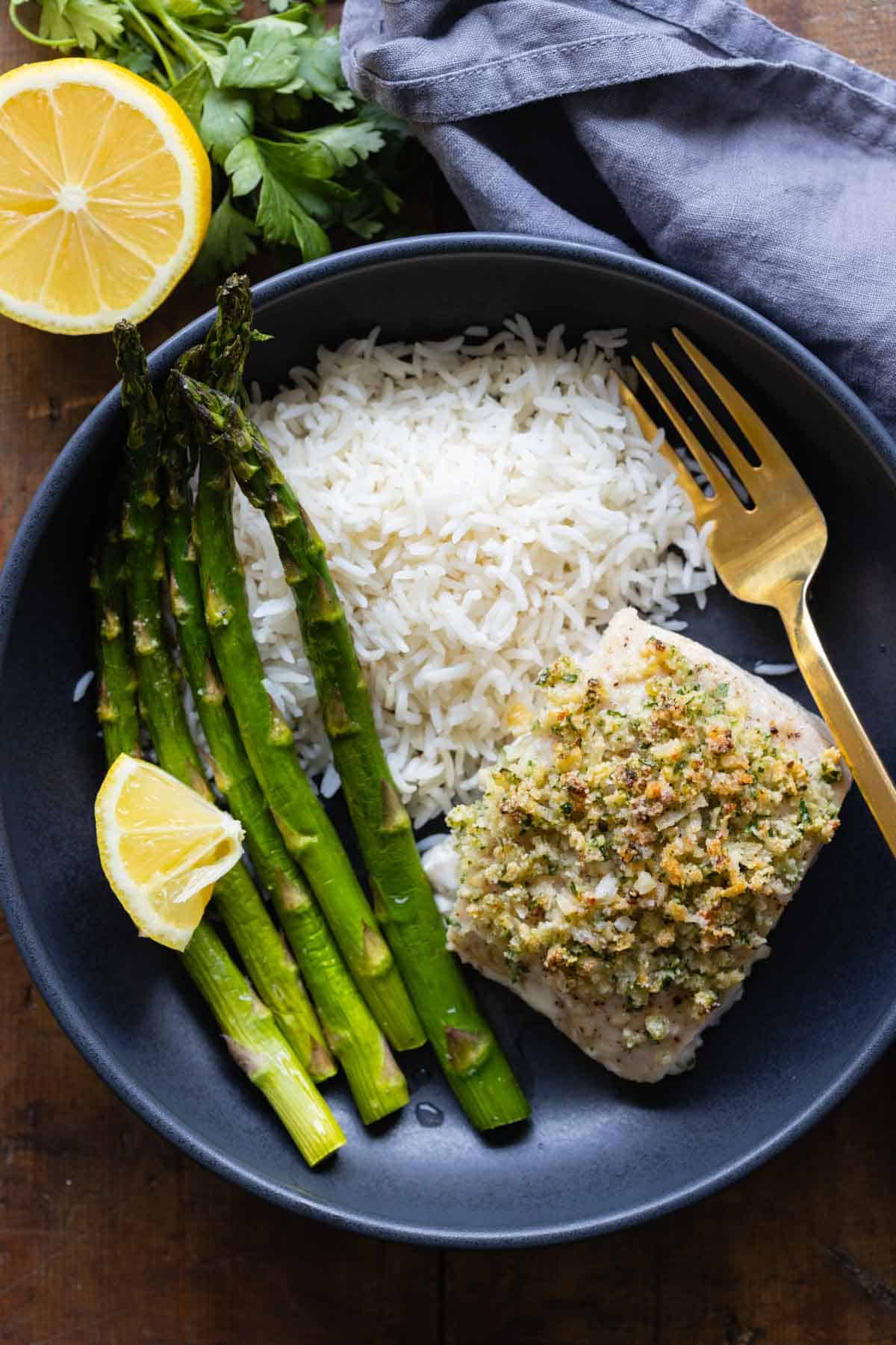Mahi Mahi Filet with Almond Parmesan Crumble in a black bowl with white rice and asparagus on the side.