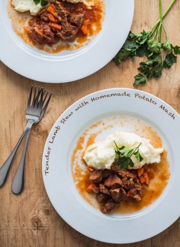 Top view of Tender Lamb Stew with Homemade Potato Mash on white plates on a wooden table with two forks, with text overlay.