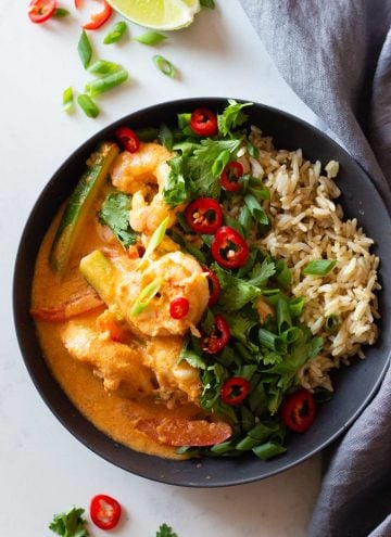 Coconut Shrimp Curry and brown rice in a grey bowl topped with herbs and chili.