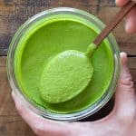 Green tahini sauce in jar and spoon lifting up green sauce.
