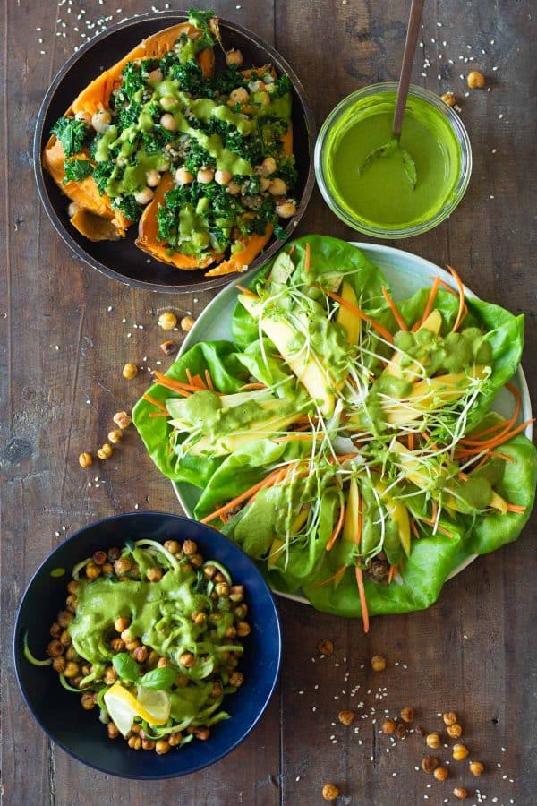 Green tahini sauce in a bowl, stuffed sweet potatoes on a plate, zucchini noodles in a bowl, lettuce tacos on a plate.
