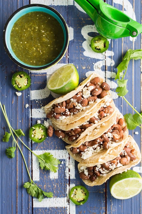 Top view of Pinto Bean Tacos with Salsa Verde and limes on a rustic wood board.