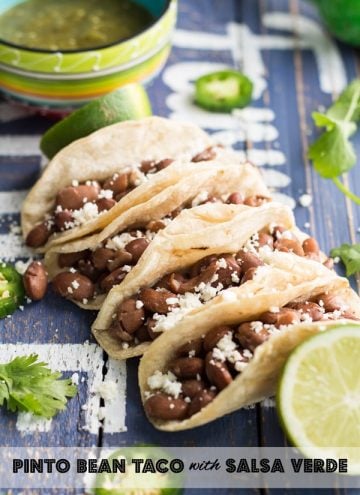 Close up of Pinto Bean Tacos with Salsa Verde on a rustic wood board with text overlay.