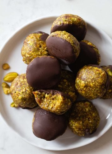 Pistachio Cookies dipped in chocolate piled on a small plate.