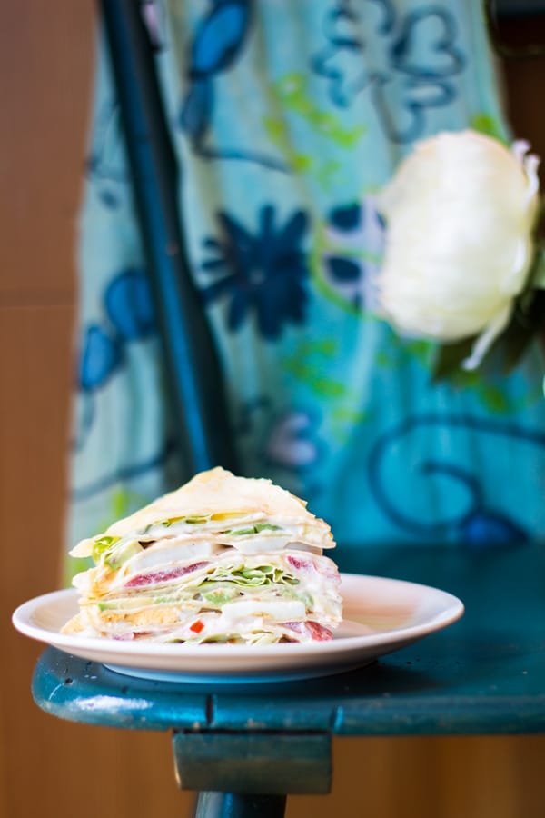 A slice of my Mum's Crepe Cake on a plate on a blue table.