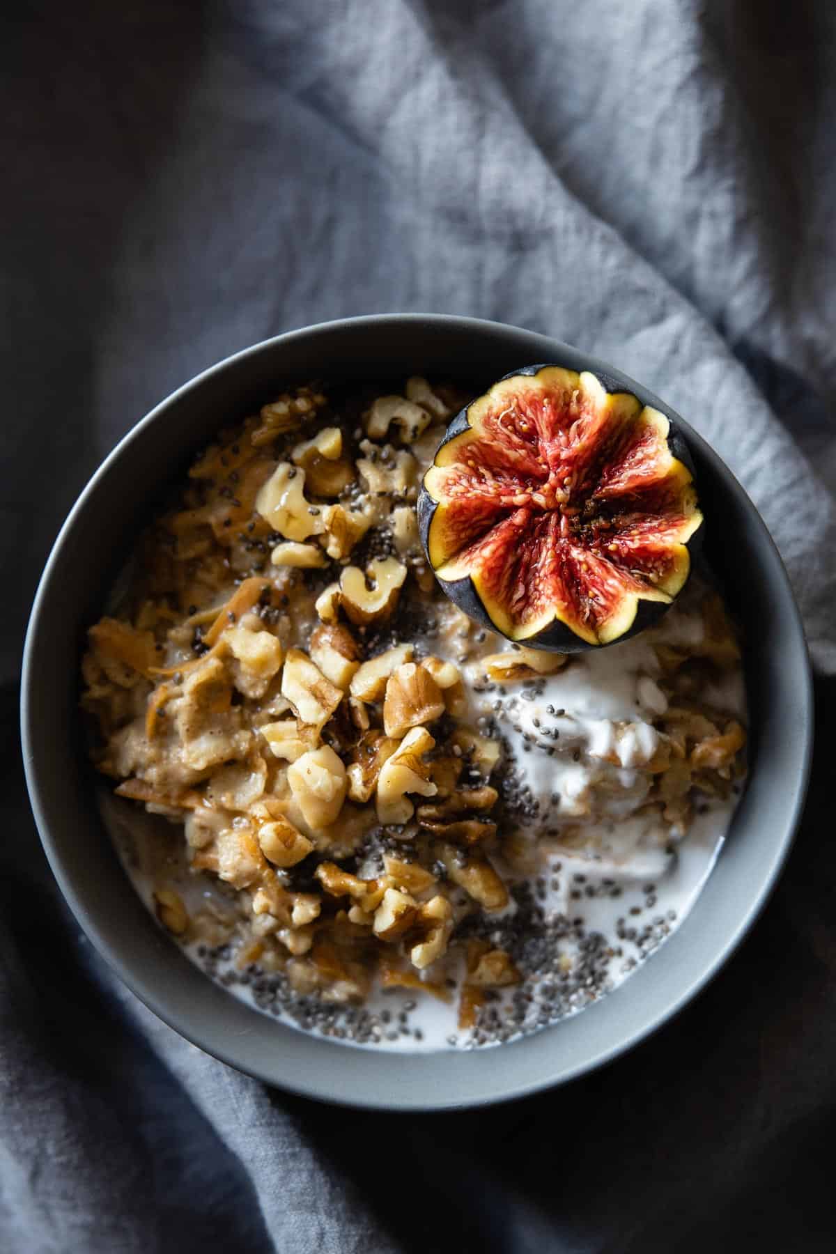 Carrot cake oatmeal in a grey bowl topped with chopped walnuts and half a fig.