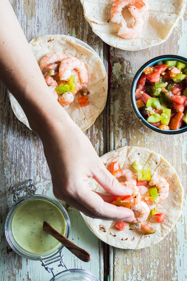 Hand sprinkling chopped tomatoes on Shrimp Tacos, a cup of Cilantro Lime Salsa and a cup of chopped tomatoes.