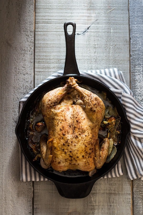 Easy Roast Chicken in skillet with a striped napkin underneath on a rustic wood board.