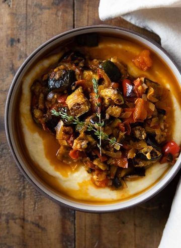Ratatouille on polenta in a bowl on a wooden table.