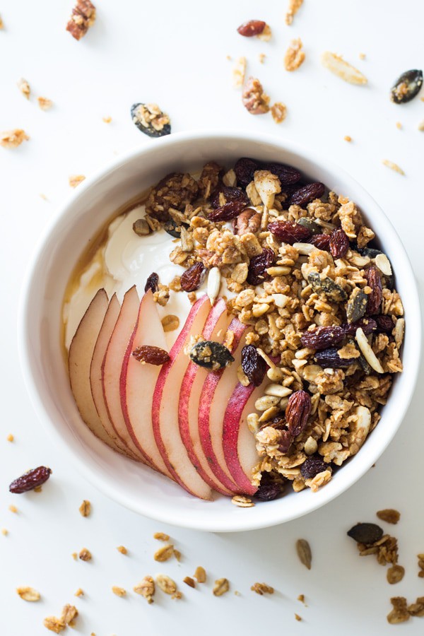 Top view of a bowl of yogurt topped with Healthy Homemade Granola, sliced apples and honey.