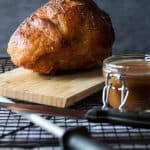 Baked Maple Mustard Ham on a wooden board and a jar of gravy.
