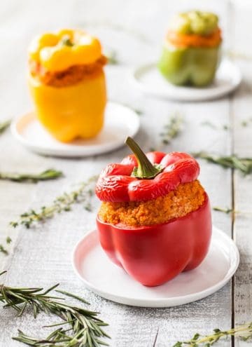 Close up of red Bulgur Stuffed Bell Pepper on a plate. Yellow and green peppers in the background.