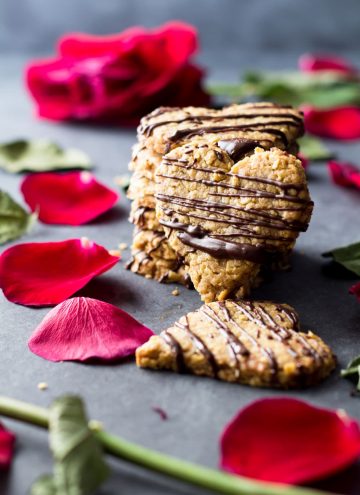 Heart-shaped spelt cookies stacked on the counter with rose petals.