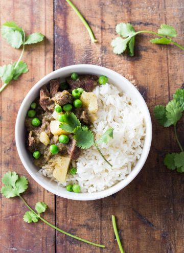 Top view of Peruvian Lamb Stew with rice and peas on a wooden board.