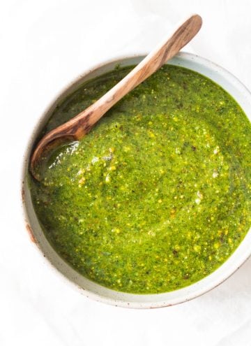 5-Minute Basil Pistachio Pesto in a white bowl with a wooden spoon.