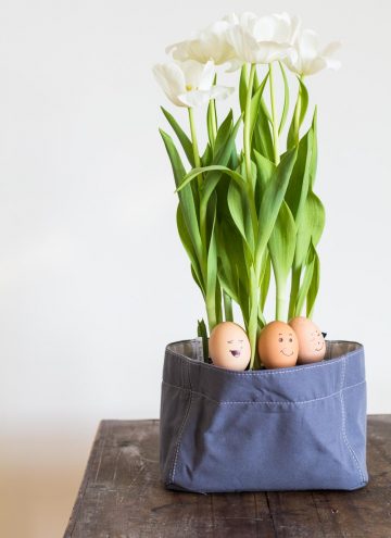 Three Easter Eggs painted with silly faces in a canvas flower pot.