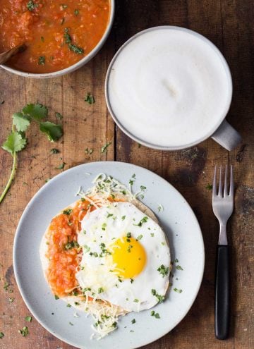 Top view of Huevo Ranchero on a plate, a fork, a cup of cappuccino, and a bowl of salsa.