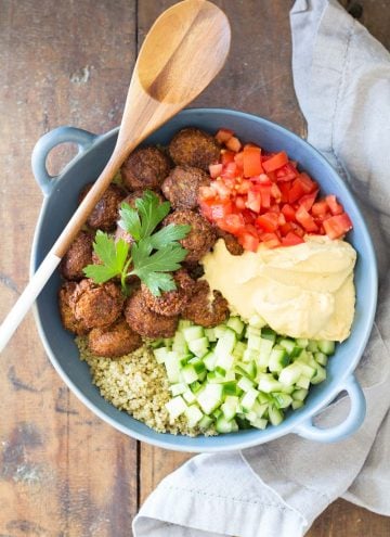 Top view of Vegan Quinoa Falafel Bowl garnished with fresh parsley, and a wooden spoon.