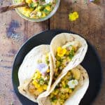 Top view of Easy Fish Tacos on a plate and a jar of Mango Salsa with a wooden spoon.
