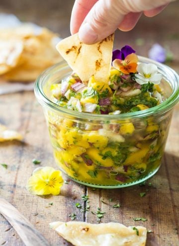 Hand dipping a tortilla chip in a Mango Salsa jar.