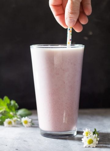 Hand holding a straw in a tall glass of Raspberry Milk.
