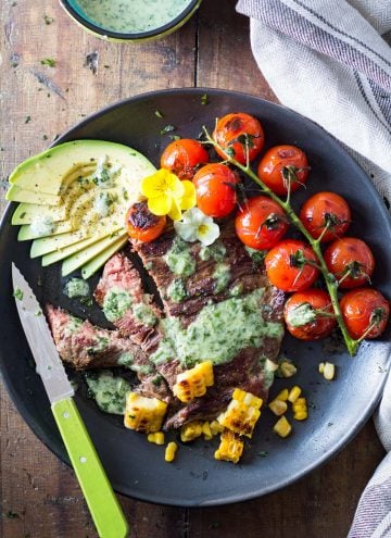 Skirt Steak with Basil Cream and Grilled Tomatoes, corn kernels and sliced avocado, a knife, and a jar of Basil Cream.