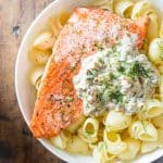 Top view of Sockeye Salmon Pasta with Shiitake mushroom sauce and fresh dill in a white bowl, and a napkin beside it.