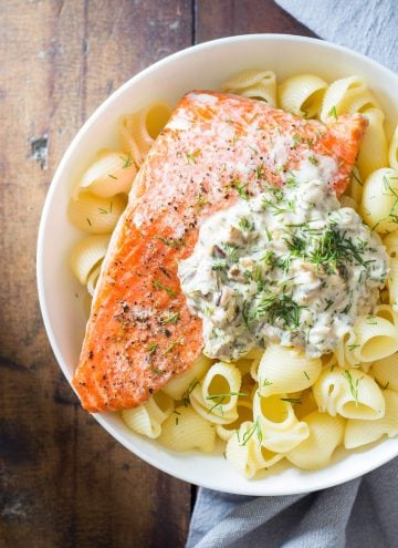 Top view of Sockeye Salmon Pasta with Shiitake mushroom sauce and fresh dill in a white bowl, and a napkin beside it.