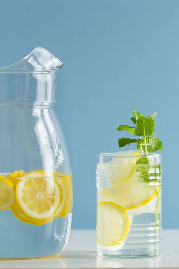 Pitcher with water and lemon slices and glass with ice and lemon slices