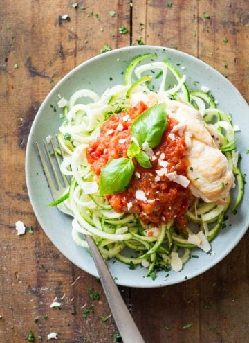 Top view of Easy Chicken Zoodles topped with tomato sauce, garnished with fresh basil leaves, and a fork.