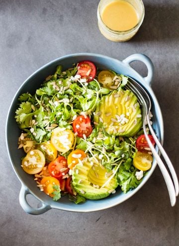 Top view of Mexican-Style Side Salad in a blue ceramic bowl with a fork and a spoon, and a jar of honey lime dressing.