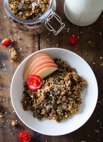 Bowl of Healthy Pumpkin Granola with apple slices, a jar with pumpkin granola, and part of a milk bottle.