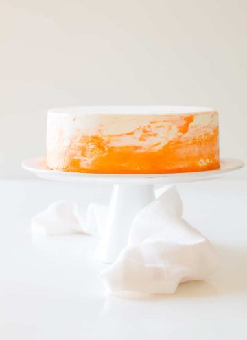 Vanilla cake with white and orange coconut cream frosting on a white cake stand.