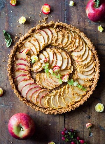 Top down view of baked apple tart on a rustic wood board and fresh apples.