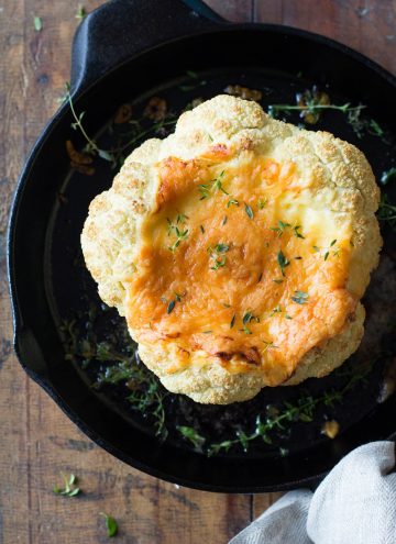 Whole roasted cauliflower with melted cheese in a cast iron pan.