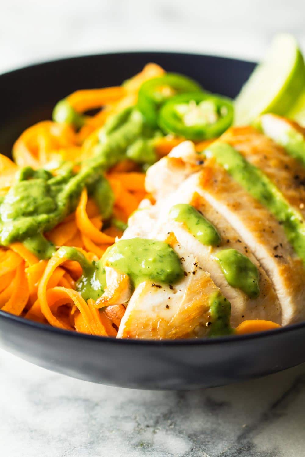 Texture of sliced chicken breast with sweet potato noodles on the side, topped with cilantro and avocado dressing. 