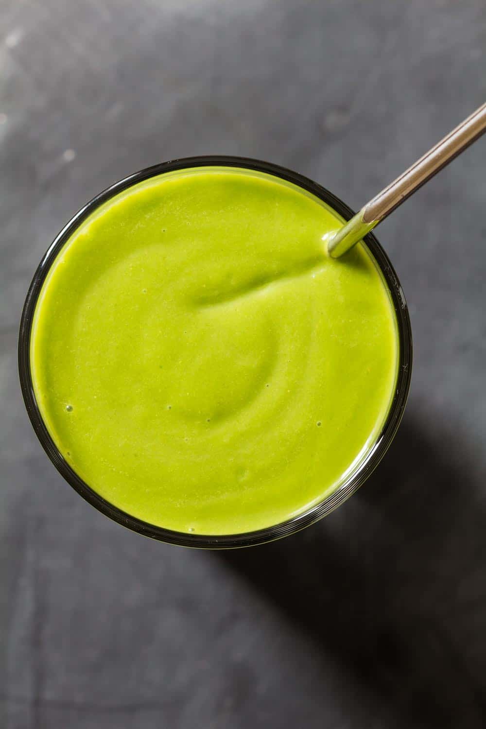 Top view of glass of spinach avocado smoothie filled to the rim with metal straw