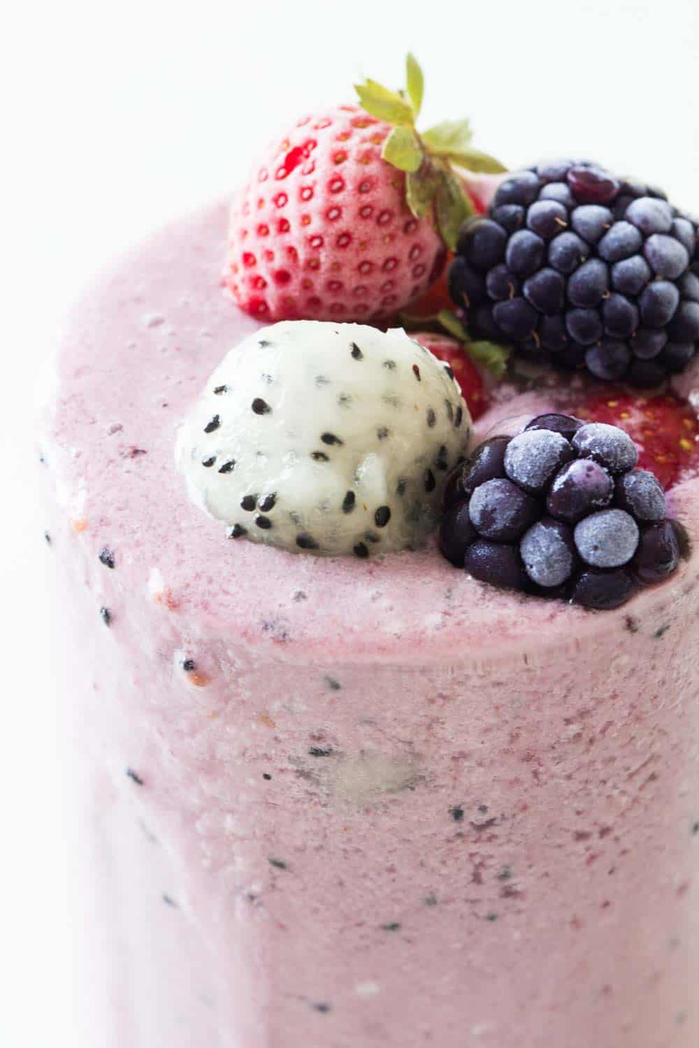 Glass filled over the rim with dragon fruit smoothie topped with a strawberry, blackberries, and a ball of dragon fruit