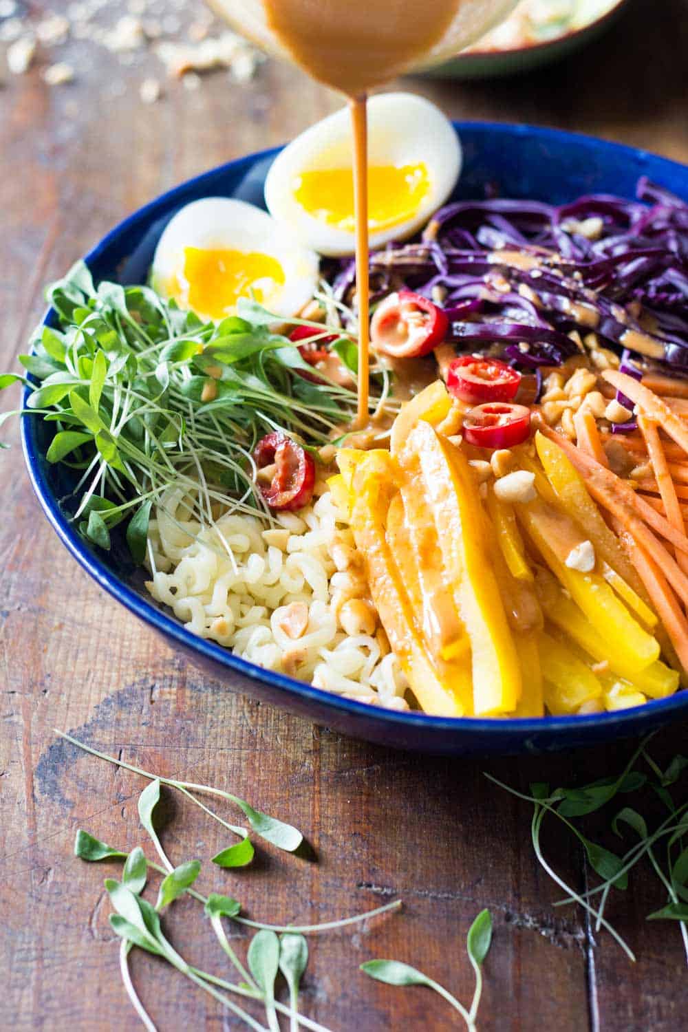 Peanut sauce being poured over ramen noodle salad served in a blue plate