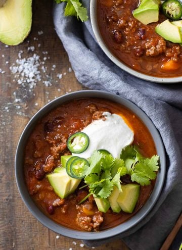 A bowl filled with chili con carne and topped with avocado, sour cream, jalapeno, and cilantro.