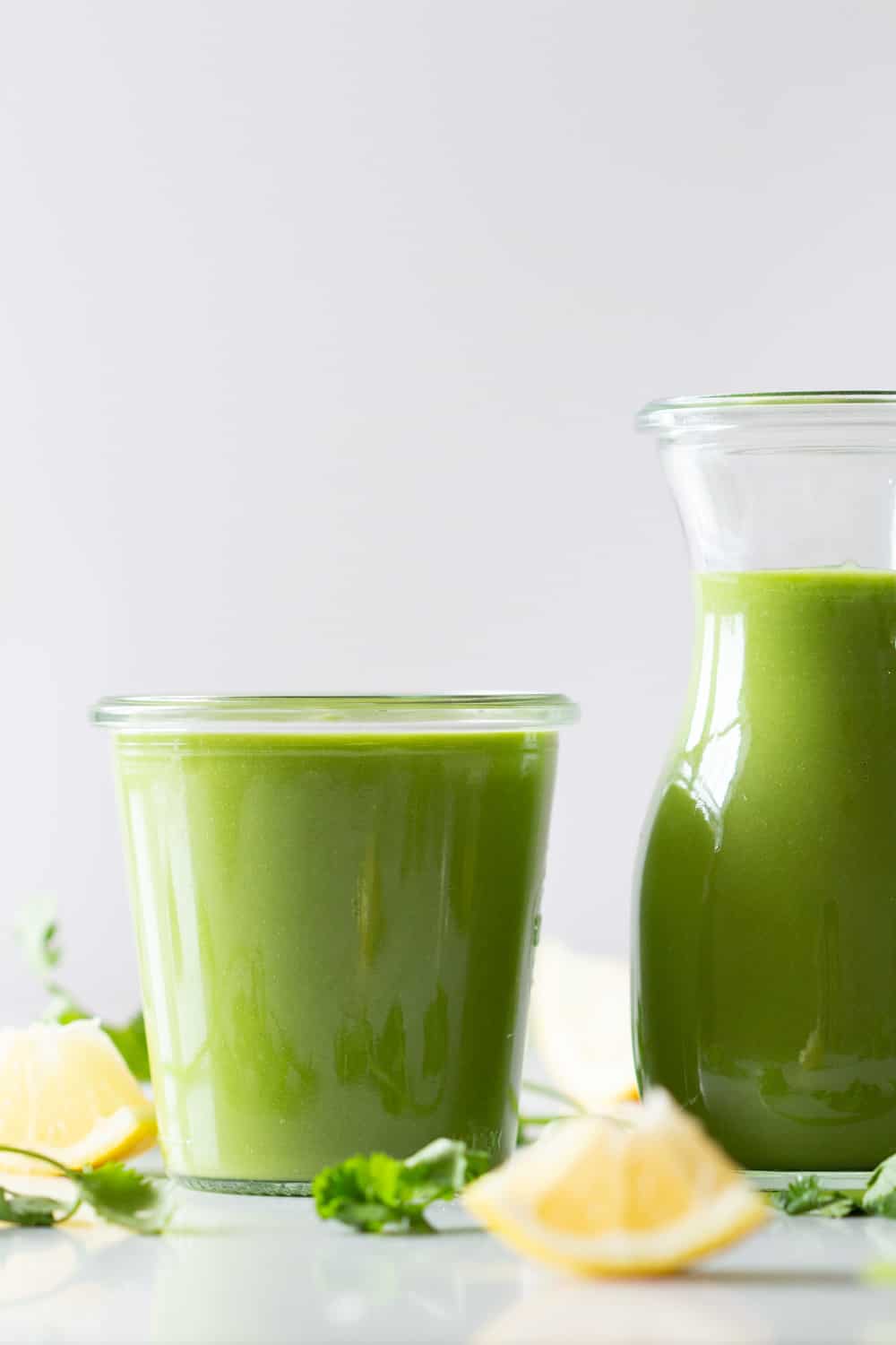 Keto Green Smoothie in a glass and keto smoothie in a small pitcher one next to the other and lemon wedges around both