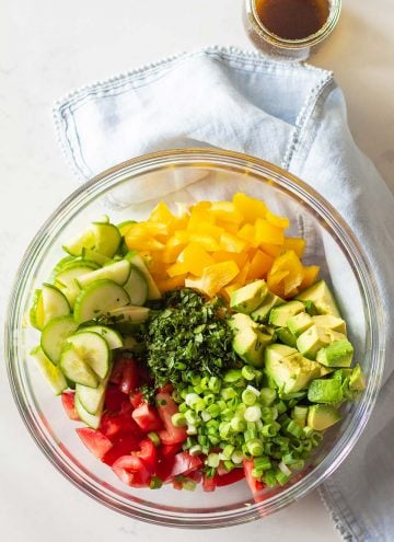 Cucumber Tomato Avocado Salad ingredients in a large glass bowl and balsamic vinaigrette in a separate glass jar