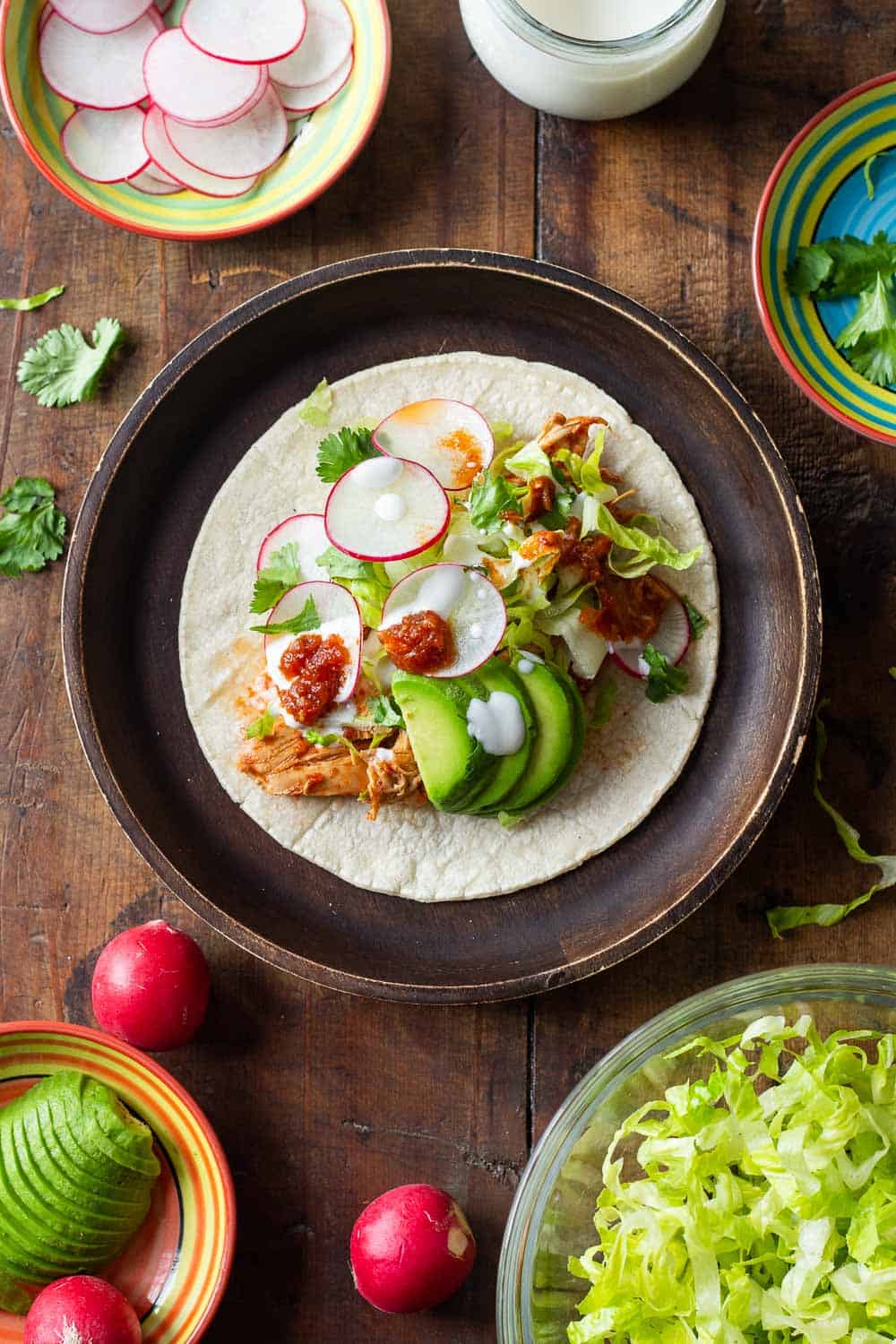 Crockpot Chicken Tacos topped with lettuce, radish, sour cream and avocado