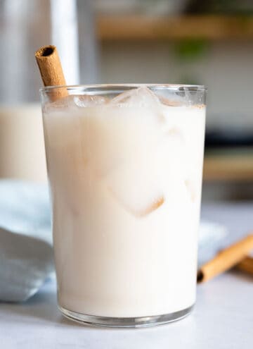 Agua de Horchata in a glass with ice and cinnamon stick sticking out.