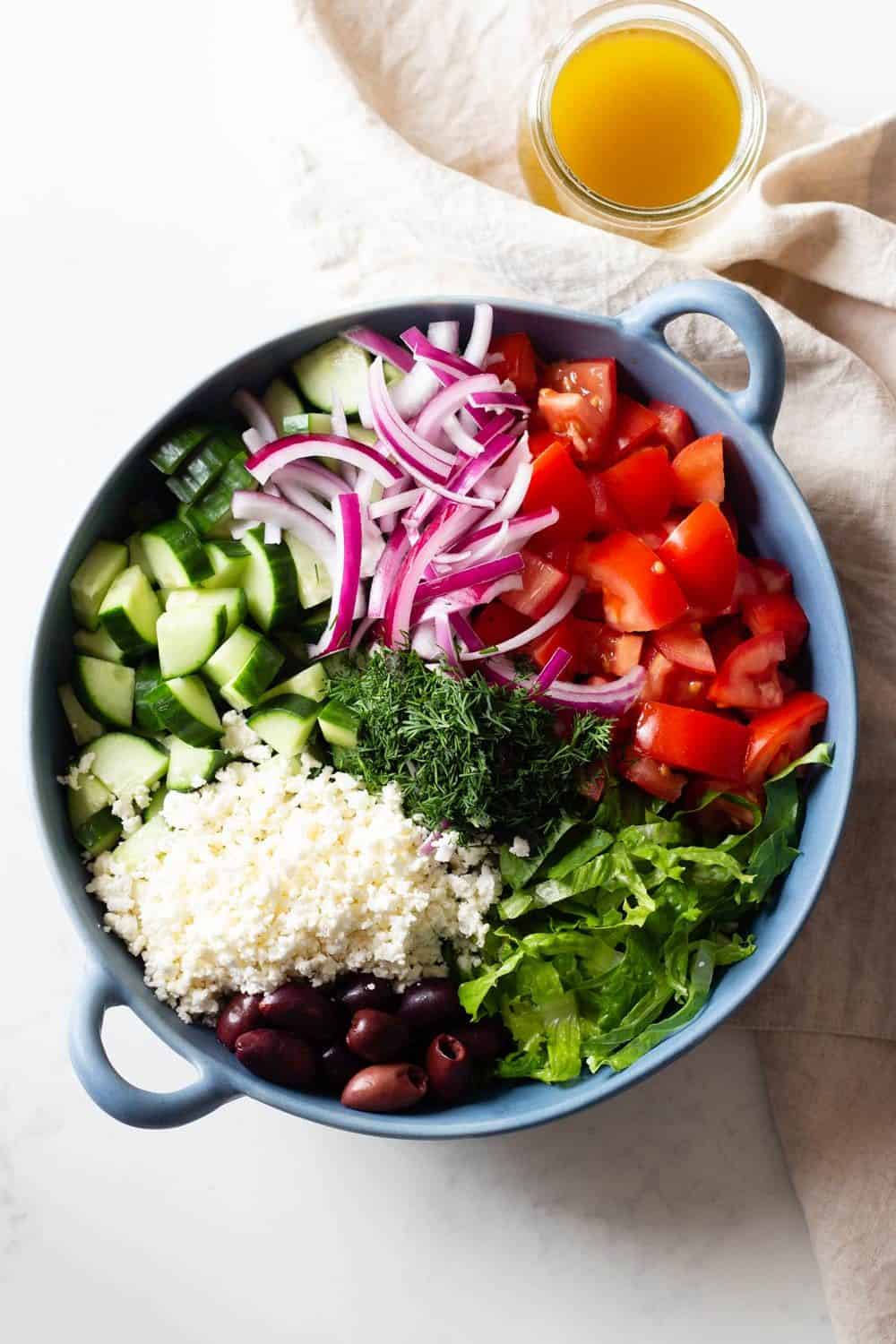 Feta Salad in a blue bowl and an open jar of dressing beside it.