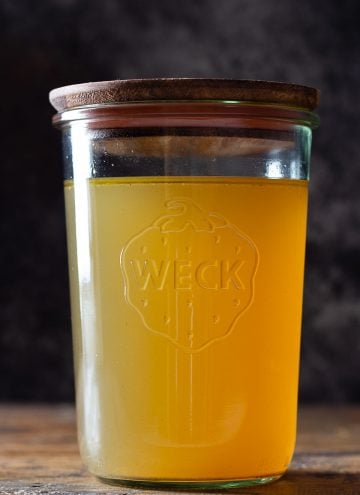 Golden chicken bone broth in a glass jar with wooden lid on top